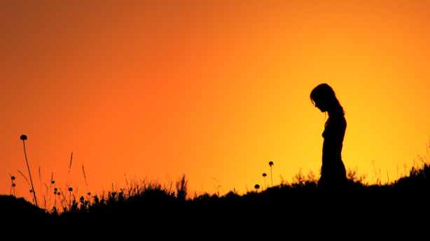 silhouette of woman standing on grass field during sunset